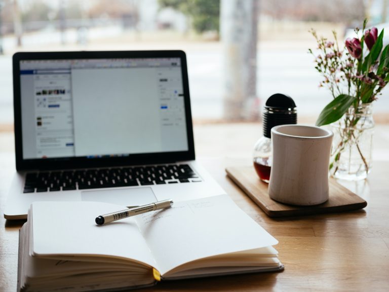 Laptop and notebook open on a table with a coffee cup